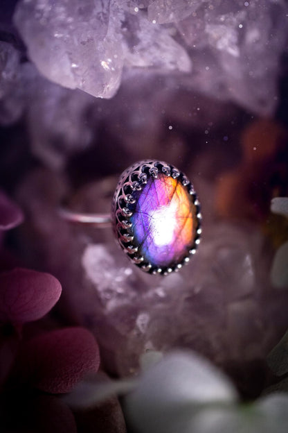 Handmade and very gothic, natural purple labradorite, sterling silver ring. This minimalist ring features a very pretty and flashy labradorite crystal that has a rich and vibrant purple colour. Around the crystal is a beautifully detail, gothic bezel that has been polished to a high lustre. The crystal is mounted on a 1.50mm ring shank. This ring would be ideal for anyone who loves jewellery and crystals, or who has a gothic and witchy style. A beautiful piece of jewellery to add to a collection