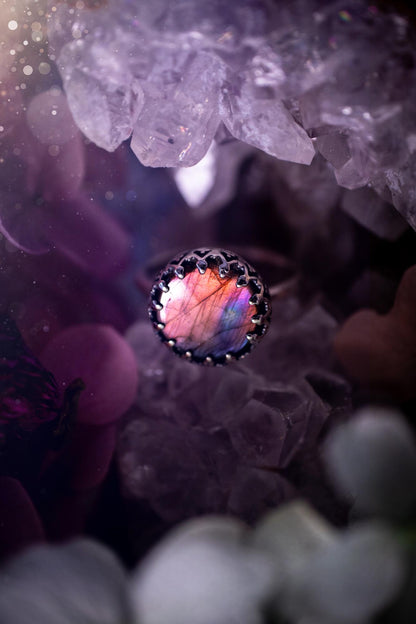 Handmade and very gothic, natural purple labradorite, sterling silver ring. This minimalist ring features a very pretty and flashy labradorite crystal that has a rich and vibrant purple colour. Around the crystal is a beautifully detail, gothic bezel that has been polished to a high lustre. The crystal is mounted on a 1.50mm ring shank. This ring would be ideal for anyone who loves jewellery and crystals, or who has a gothic and witchy style. A beautiful piece of jewellery to add to a collection