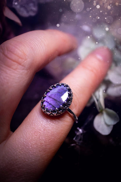 Handmade and very gothic, natural purple labradorite, sterling silver ring. This minimalist ring features a very pretty and flashy labradorite crystal that has a rich and vibrant purple colour. Around the crystal is a beautifully detail, gothic bezel that has been polished to a high lustre. The crystal is mounted on a 1.50mm ring shank. This ring would be ideal for anyone who loves jewellery and crystals, or who has a gothic and witchy style. A beautiful piece of jewellery to add to a collection