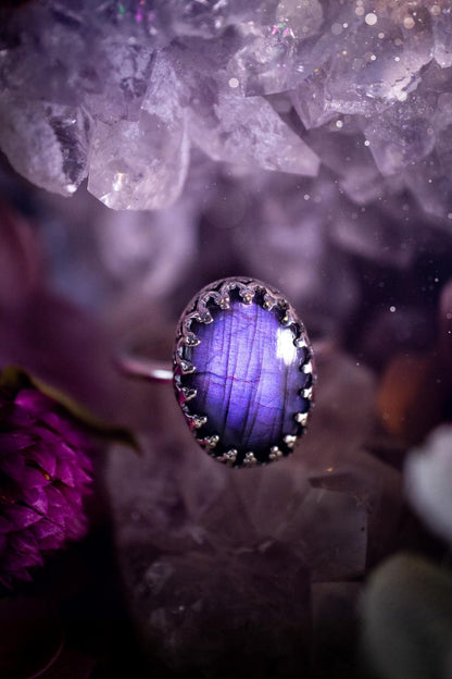 Handmade and very gothic, natural purple labradorite, sterling silver ring. This minimalist ring features a very pretty and flashy labradorite crystal that has a rich and vibrant purple colour. Around the crystal is a beautifully detail, gothic bezel that has been polished to a high lustre. The crystal is mounted on a 1.50mm ring shank. This ring would be ideal for anyone who loves jewellery and crystals, or who has a gothic and witchy style. A beautiful piece of jewellery to add to a collection