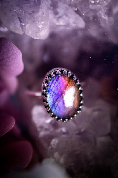 Handmade and very gothic, natural purple labradorite, sterling silver ring. This minimalist ring features a very pretty and flashy labradorite crystal that has a rich and vibrant purple colour. Around the crystal is a beautifully detail, gothic bezel that has been polished to a high lustre. The crystal is mounted on a 1.50mm ring shank. This ring would be ideal for anyone who loves jewellery and crystals, or who has a gothic and witchy style. A beautiful piece of jewellery to add to a collection