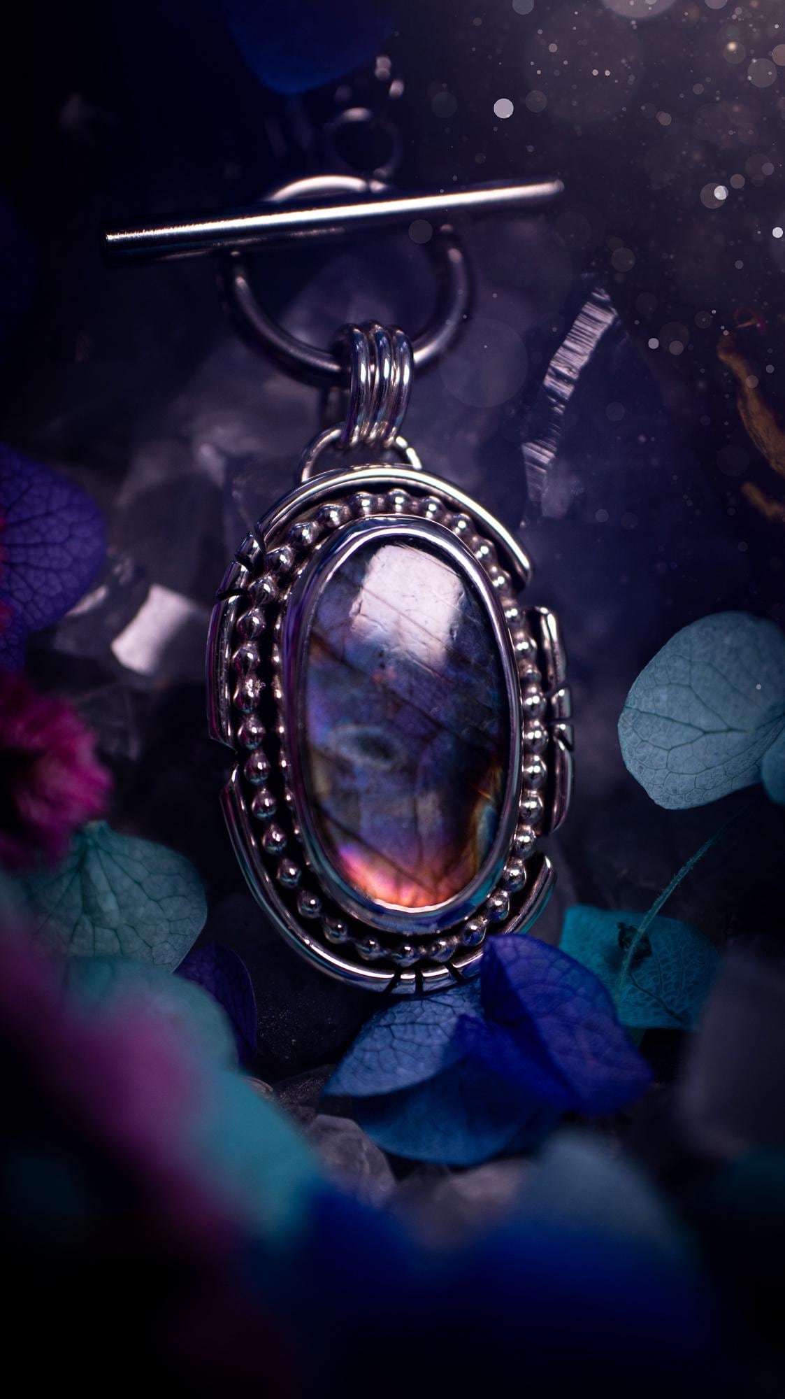 Beautifully handmade, amulet pendant necklace which features the most beautiful rainbow coloured, labradorite spectrolite crystal. This pendant has been handcrafted using a mix of fine and sterling silver. It features a smooth bezel with beaded, and hand carved smooth wire around the stone making this piece totally bespoke and one of a kind. The labradorite has an array of beautiful purples, blues and pinks. This pendant would be suitable for any crystal and jewellery lover, gothic and hippy!