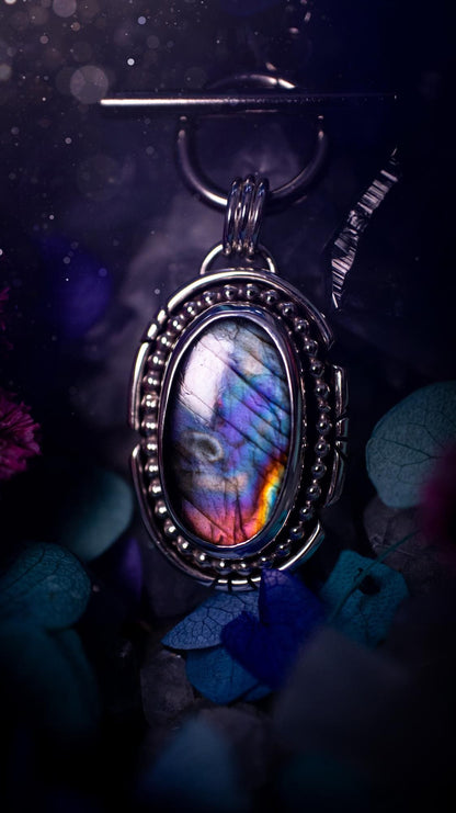 Beautifully handmade, amulet pendant necklace which features the most beautiful rainbow coloured, labradorite spectrolite crystal. This pendant has been handcrafted using a mix of fine and sterling silver. It features a smooth bezel with beaded, and hand carved smooth wire around the stone making this piece totally bespoke and one of a kind. The labradorite has an array of beautiful purples, blues and pinks. This pendant would be suitable for any crystal and jewellery lover, gothic and hippy!