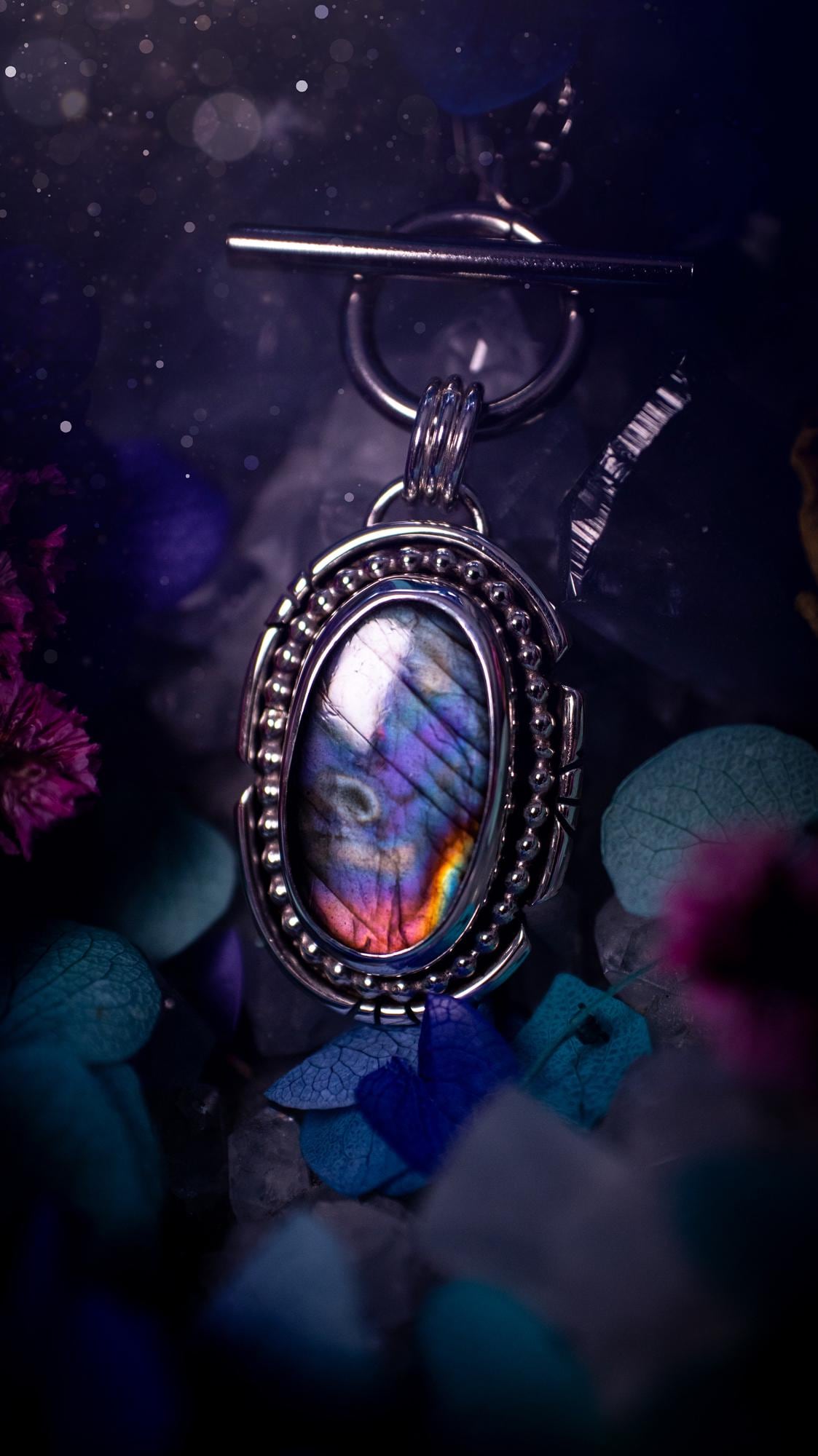 Beautifully handmade, amulet pendant necklace which features the most beautiful rainbow coloured, labradorite spectrolite crystal. This pendant has been handcrafted using a mix of fine and sterling silver. It features a smooth bezel with beaded, and hand carved smooth wire around the stone making this piece totally bespoke and one of a kind. The labradorite has an array of beautiful purples, blues and pinks. This pendant would be suitable for any crystal and jewellery lover, gothic and hippy!