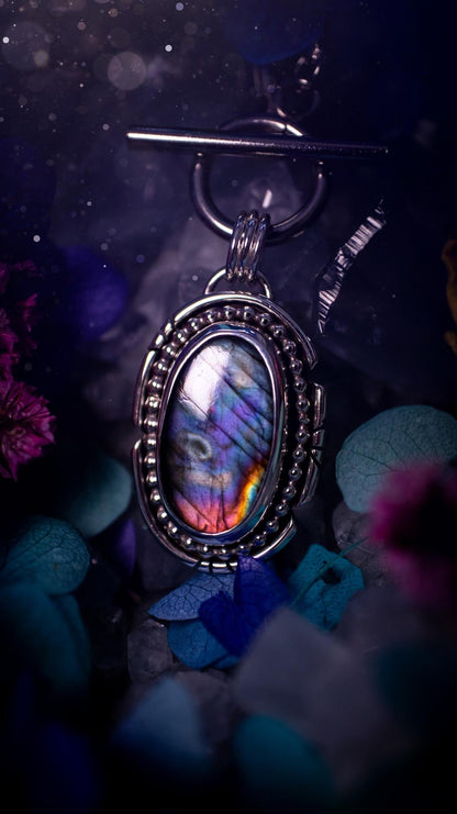 Beautifully handmade, amulet pendant necklace which features the most beautiful rainbow coloured, labradorite spectrolite crystal. This pendant has been handcrafted using a mix of fine and sterling silver. It features a smooth bezel with beaded, and hand carved smooth wire around the stone making this piece totally bespoke and one of a kind. The labradorite has an array of beautiful purples, blues and pinks. This pendant would be suitable for any crystal and jewellery lover, gothic and hippy!