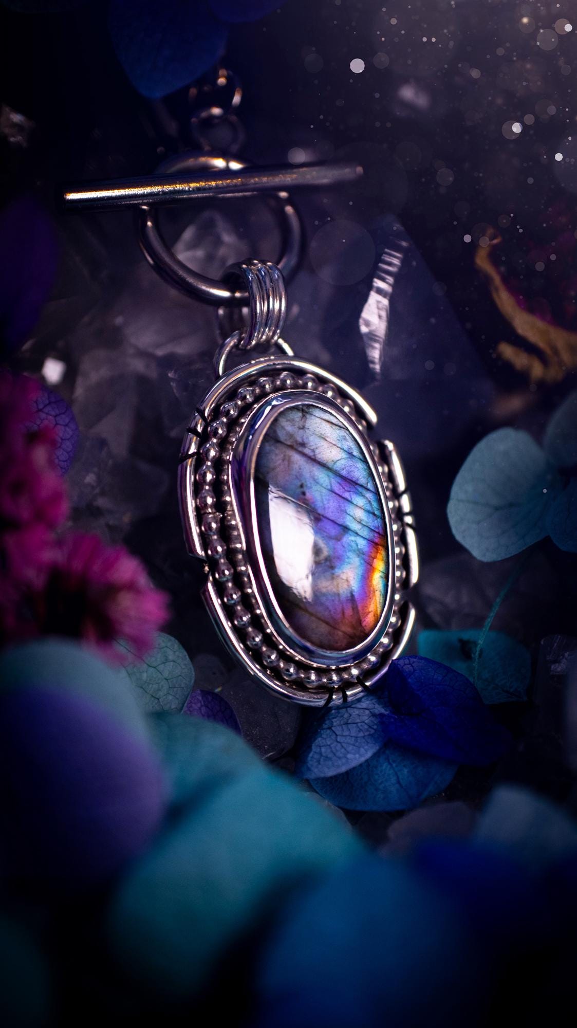 Beautifully handmade, amulet pendant necklace which features the most beautiful rainbow coloured, labradorite spectrolite crystal. This pendant has been handcrafted using a mix of fine and sterling silver. It features a smooth bezel with beaded, and hand carved smooth wire around the stone making this piece totally bespoke and one of a kind. The labradorite has an array of beautiful purples, blues and pinks. This pendant would be suitable for any crystal and jewellery lover, gothic and hippy!