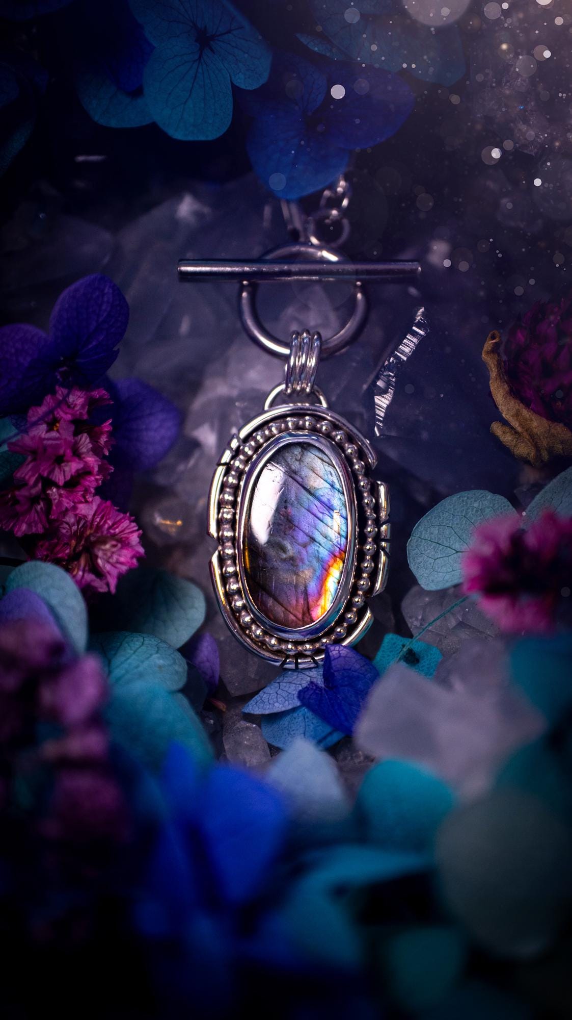 Beautifully handmade, amulet pendant necklace which features the most beautiful rainbow coloured, labradorite spectrolite crystal. This pendant has been handcrafted using a mix of fine and sterling silver. It features a smooth bezel with beaded, and hand carved smooth wire around the stone making this piece totally bespoke and one of a kind. The labradorite has an array of beautiful purples, blues and pinks. This pendant would be suitable for any crystal and jewellery lover, gothic and hippy!