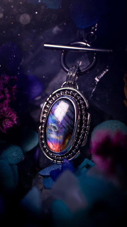 Beautifully handmade, amulet pendant necklace which features the most beautiful rainbow coloured, labradorite spectrolite crystal. This pendant has been handcrafted using a mix of fine and sterling silver. It features a smooth bezel with beaded, and hand carved smooth wire around the stone making this piece totally bespoke and one of a kind. The labradorite has an array of beautiful purples, blues and pinks. This pendant would be suitable for any crystal and jewellery lover, gothic and hippy!