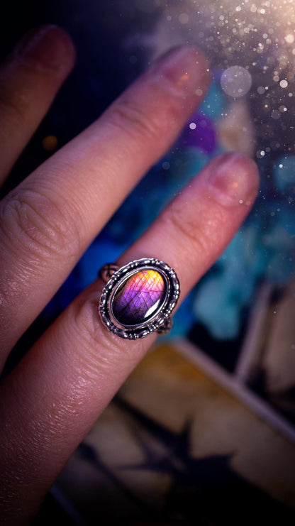 Handmade and very gothic, natural purple labradorite, sterling silver ring. This minimalist ring features a very pretty and flashy labradorite crystal that has a rich and vibrant purple colour. Around the crystal is a beautifully detail, gothic bezel that has been polished to a high lustre. The crystal is mounted on stamped ring shank. This ring would be ideal for anyone who loves jewellery and crystals, or who has a gothic and witchy style. A beautiful piece of jewellery to add to a collection