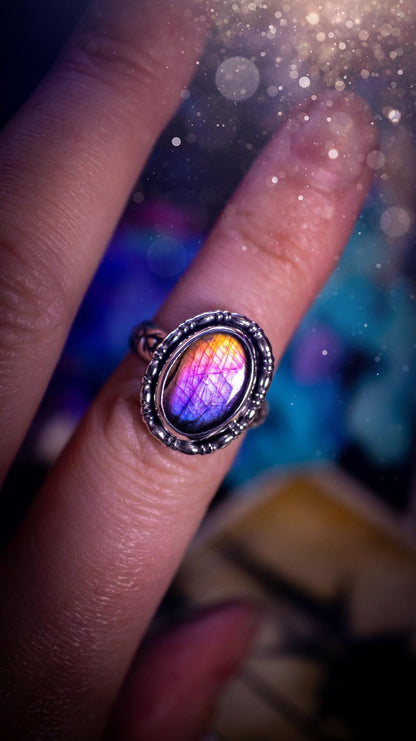 Handmade and very gothic, natural purple labradorite, sterling silver ring. This minimalist ring features a very pretty and flashy labradorite crystal that has a rich and vibrant purple colour. Around the crystal is a beautifully detail, gothic bezel that has been polished to a high lustre. The crystal is mounted on stamped ring shank. This ring would be ideal for anyone who loves jewellery and crystals, or who has a gothic and witchy style. A beautiful piece of jewellery to add to a collection