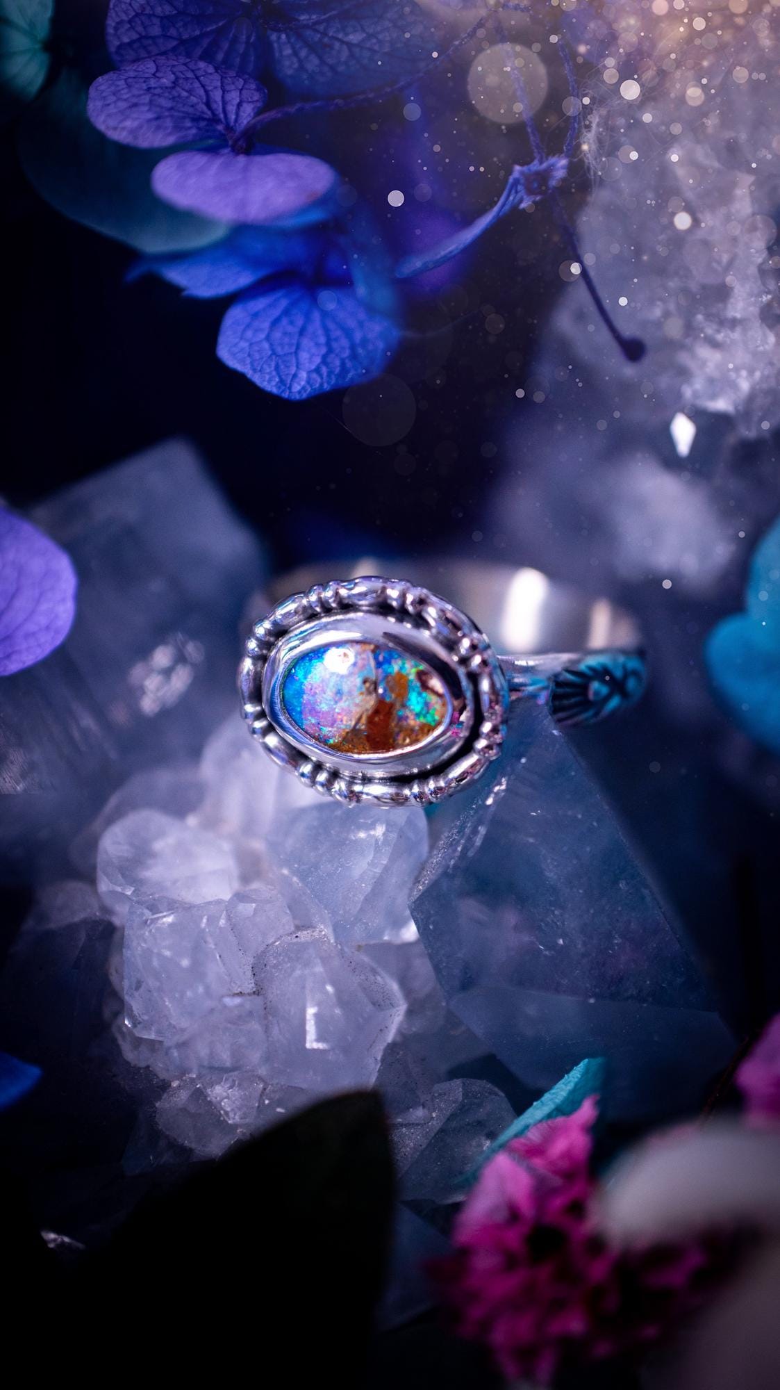 One of a kind and handmade, Australian boulder opal, bohemian ring. This stunning ring has been handcrafted using a mix of fine and sterling silver. Featuring a small, yet totally stunning and vibrant Australian boulder opal full of blues, purples, and green sparkles. Around the smooth bezel is some pretty gallery wire. The ring shank has also been stamped with a bohemian pattern. This one off piece is ideal for any crystal and jewellery lover who is seeking a piece that has no other the same!