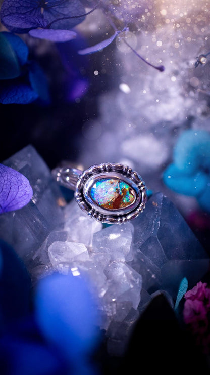 One of a kind and handmade, Australian boulder opal, bohemian ring. This stunning ring has been handcrafted using a mix of fine and sterling silver. Featuring a small, yet totally stunning and vibrant Australian boulder opal full of blues, purples, and green sparkles. Around the smooth bezel is some pretty gallery wire. The ring shank has also been stamped with a bohemian pattern. This one off piece is ideal for any crystal and jewellery lover who is seeking a piece that has no other the same!