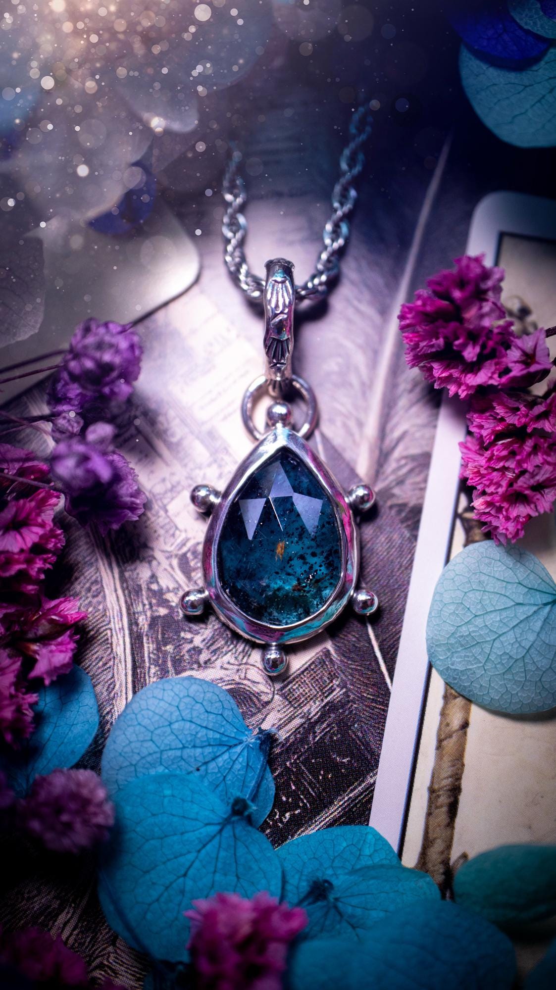 One of a kind, stunning and natural, mossy, sea blue kyanite, pendant necklace. This pendant has been handcrafted using a mix of fine and sterling silver. Featuring a natural and gorgeous, deep teal blue kyanite that has mossy inclusions and rainbows! The stone is rose cut for an extra sparkle. Around the smooth bezel is small ball details, with a bohemian stamped pattern bail. This piece would be ideal for anyone who loves jewellery, crystals or both! Bohemian and hippy jewellery for the soul.