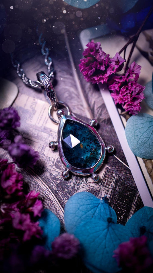 One of a kind, stunning and natural, mossy, sea blue kyanite, pendant necklace. This pendant has been handcrafted using a mix of fine and sterling silver. Featuring a natural and gorgeous, deep teal blue kyanite that has mossy inclusions and rainbows! The stone is rose cut for an extra sparkle. Around the smooth bezel is small ball details, with a bohemian stamped pattern bail. This piece would be ideal for anyone who loves jewellery, crystals or both! Bohemian and hippy jewellery for the soul.