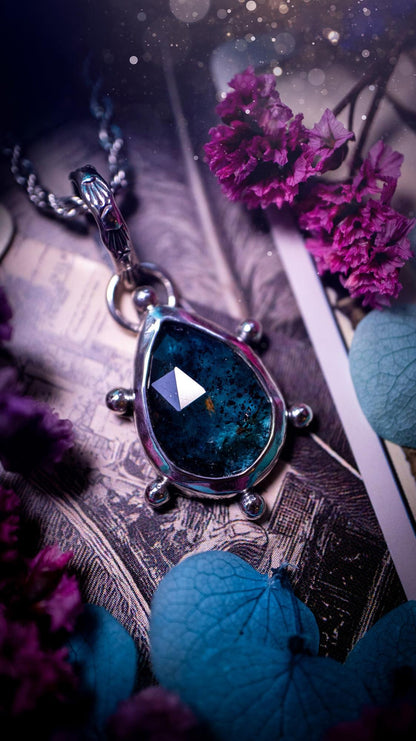 One of a kind, stunning and natural, mossy, sea blue kyanite, pendant necklace. This pendant has been handcrafted using a mix of fine and sterling silver. Featuring a natural and gorgeous, deep teal blue kyanite that has mossy inclusions and rainbows! The stone is rose cut for an extra sparkle. Around the smooth bezel is small ball details, with a bohemian stamped pattern bail. This piece would be ideal for anyone who loves jewellery, crystals or both! Bohemian and hippy jewellery for the soul.