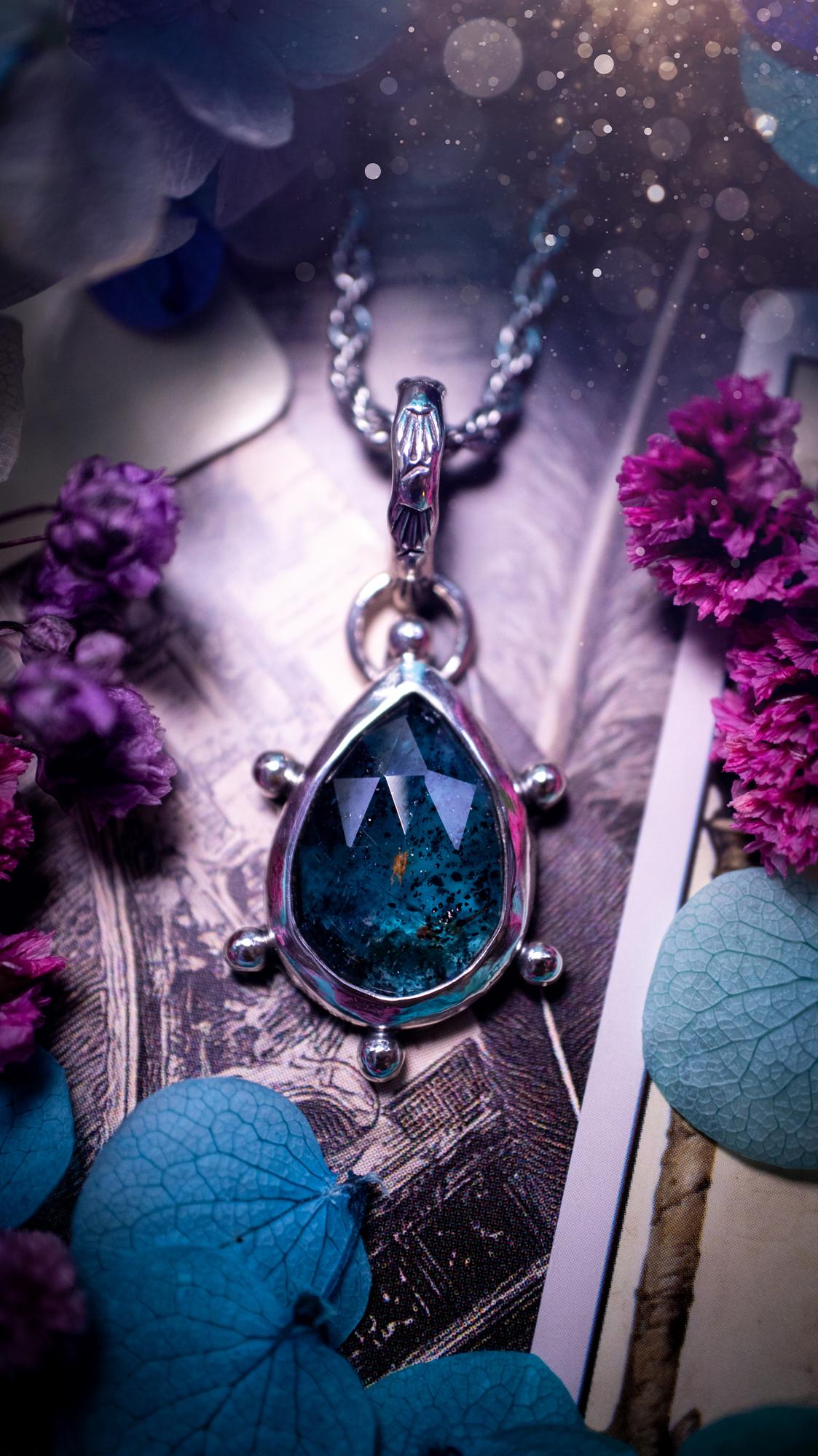One of a kind, stunning and natural, mossy, sea blue kyanite, pendant necklace. This pendant has been handcrafted using a mix of fine and sterling silver. Featuring a natural and gorgeous, deep teal blue kyanite that has mossy inclusions and rainbows! The stone is rose cut for an extra sparkle. Around the smooth bezel is small ball details, with a bohemian stamped pattern bail. This piece would be ideal for anyone who loves jewellery, crystals or both! Bohemian and hippy jewellery for the soul.