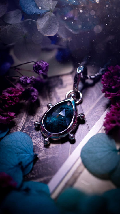 One of a kind, stunning and natural, mossy, sea blue kyanite, pendant necklace. This pendant has been handcrafted using a mix of fine and sterling silver. Featuring a natural and gorgeous, deep teal blue kyanite that has mossy inclusions and rainbows! The stone is rose cut for an extra sparkle. Around the smooth bezel is small ball details, with a bohemian stamped pattern bail. This piece would be ideal for anyone who loves jewellery, crystals or both! Bohemian and hippy jewellery for the soul.