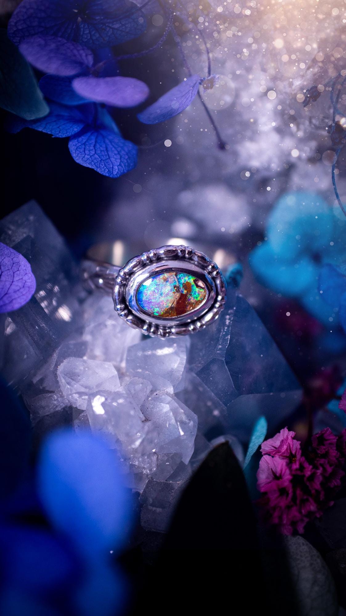 One of a kind and handmade, Australian boulder opal, bohemian ring. This stunning ring has been handcrafted using a mix of fine and sterling silver. Featuring a small, yet totally stunning and vibrant Australian boulder opal full of blues, purples, and green sparkles. Around the smooth bezel is some pretty gallery wire. The ring shank has also been stamped with a bohemian pattern. This one off piece is ideal for any crystal and jewellery lover who is seeking a piece that has no other the same!