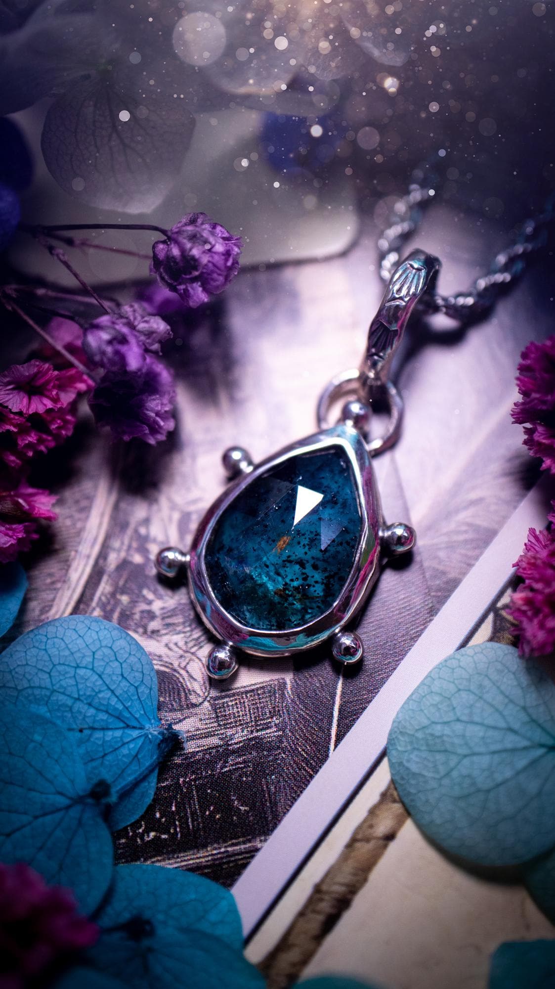 One of a kind, stunning and natural, mossy, sea blue kyanite, pendant necklace. This pendant has been handcrafted using a mix of fine and sterling silver. Featuring a natural and gorgeous, deep teal blue kyanite that has mossy inclusions and rainbows! The stone is rose cut for an extra sparkle. Around the smooth bezel is small ball details, with a bohemian stamped pattern bail. This piece would be ideal for anyone who loves jewellery, crystals or both! Bohemian and hippy jewellery for the soul.