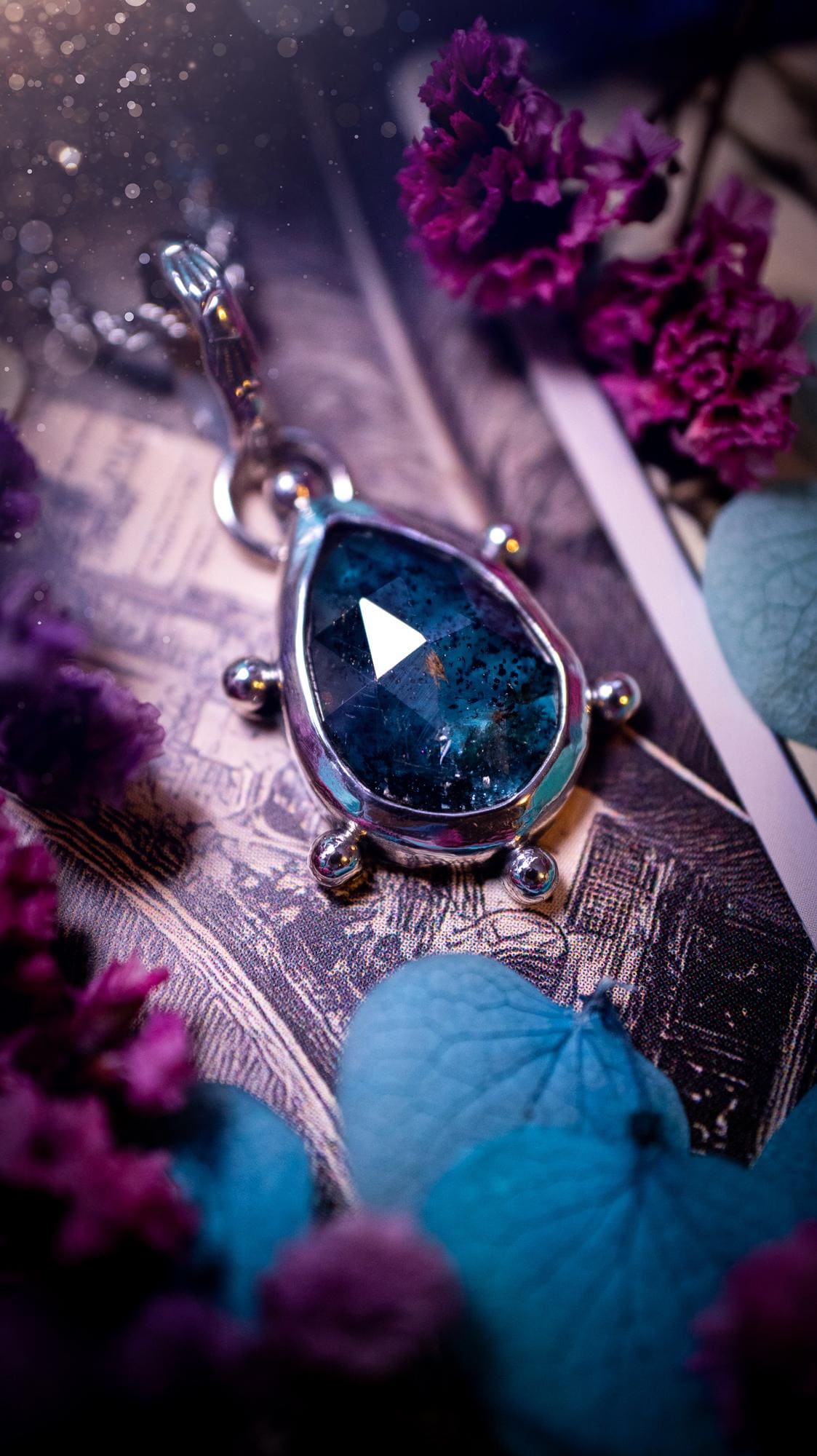 One of a kind, stunning and natural, mossy, sea blue kyanite, pendant necklace. This pendant has been handcrafted using a mix of fine and sterling silver. Featuring a natural and gorgeous, deep teal blue kyanite that has mossy inclusions and rainbows! The stone is rose cut for an extra sparkle. Around the smooth bezel is small ball details, with a bohemian stamped pattern bail. This piece would be ideal for anyone who loves jewellery, crystals or both! Bohemian and hippy jewellery for the soul.