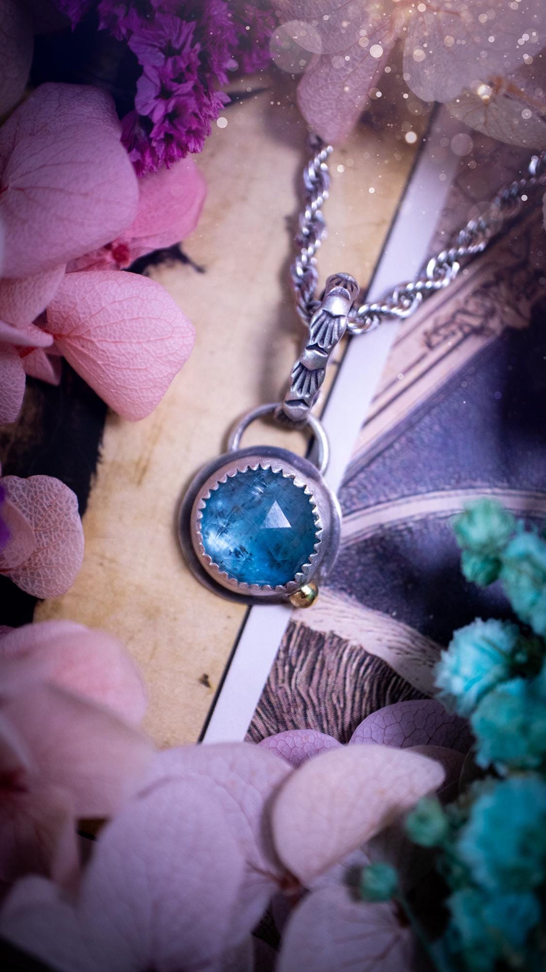 Handmade Paraiba kyanite pendant set in sterling silver with a satin brushed finish. The natural kyanite gemstone displays vibrant ocean-blue tones with a luminous glow. Finished with a polished brass golden ball accent and a decorative patterned bail. Bohemian, gothic and witchy style crystal jewellery, perfect as a unique gift or standout everyday piece