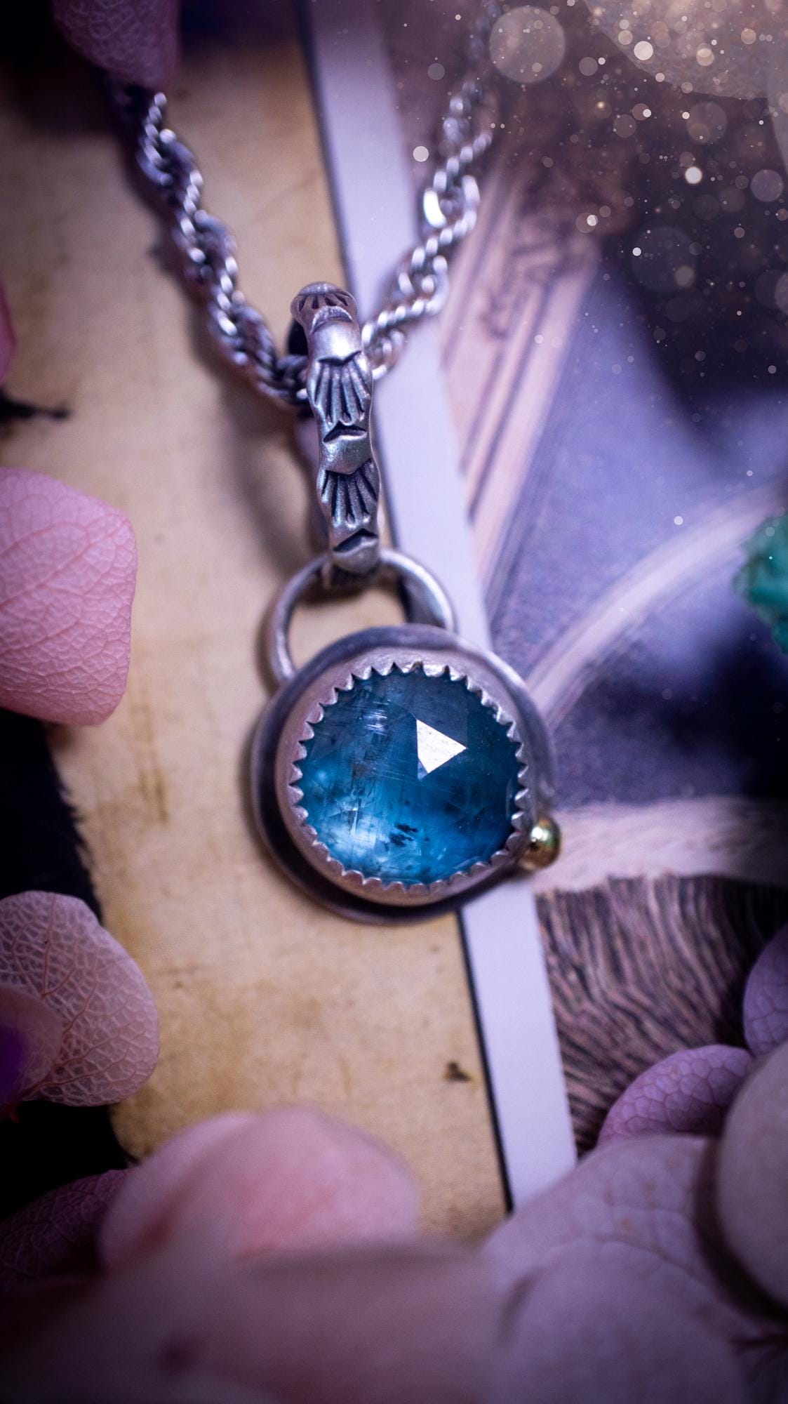 Handmade Paraiba kyanite pendant set in sterling silver with a satin brushed finish. The natural kyanite gemstone displays vibrant ocean-blue tones with a luminous glow. Finished with a polished brass golden ball accent and a decorative patterned bail. Bohemian, gothic and witchy style crystal jewellery, perfect as a unique gift or standout everyday piece
