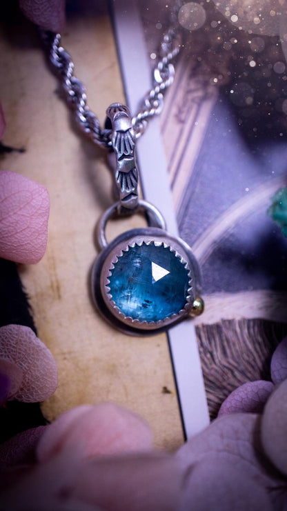 Handmade Paraiba kyanite pendant set in sterling silver with a satin brushed finish. The natural kyanite gemstone displays vibrant ocean-blue tones with a luminous glow. Finished with a polished brass golden ball accent and a decorative patterned bail. Bohemian, gothic and witchy style crystal jewellery, perfect as a unique gift or standout everyday piece