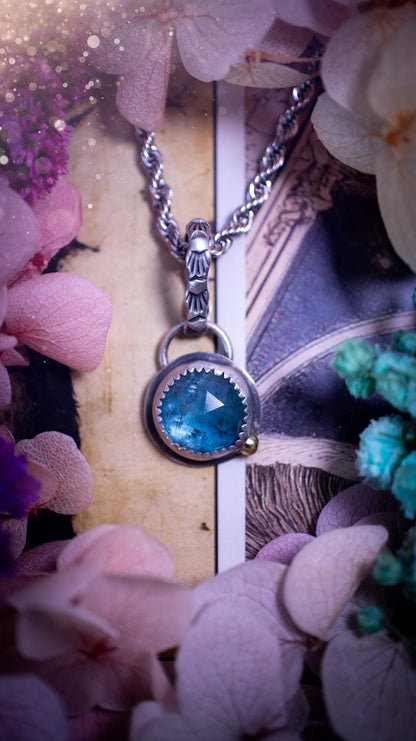 Handmade Paraiba kyanite pendant set in sterling silver with a satin brushed finish. The natural kyanite gemstone displays vibrant ocean-blue tones with a luminous glow. Finished with a polished brass golden ball accent and a decorative patterned bail. Bohemian, gothic and witchy style crystal jewellery, perfect as a unique gift or standout everyday piece