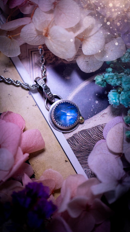 Handmade rainbow moonstone pendant set in sterling silver with a satin brushed finish. The natural moonstone gemstone shows a soft blue flash that shifts beautifully in the light. Finished with a polished brass golden ball accent and a decorative patterned bail. Bohemian, gothic and witchy style crystal jewellery, perfect as a unique gift or elegant everyday piece.