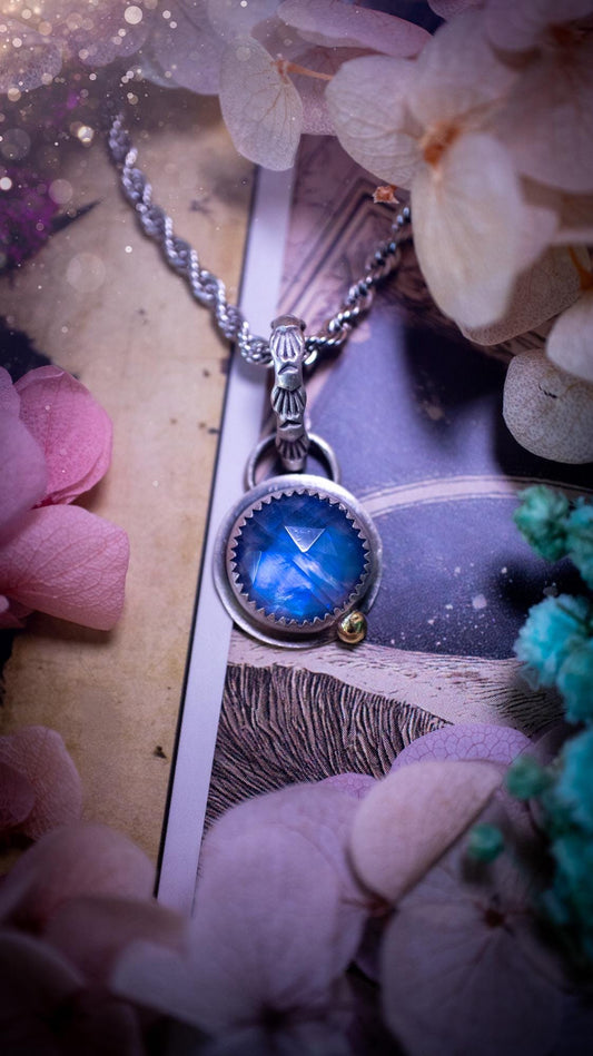 Handmade rainbow moonstone pendant set in sterling silver with a satin brushed finish. The natural moonstone gemstone shows a soft blue flash that shifts beautifully in the light. Finished with a polished brass golden ball accent and a decorative patterned bail. Bohemian, gothic and witchy style crystal jewellery, perfect as a unique gift or elegant everyday piece.