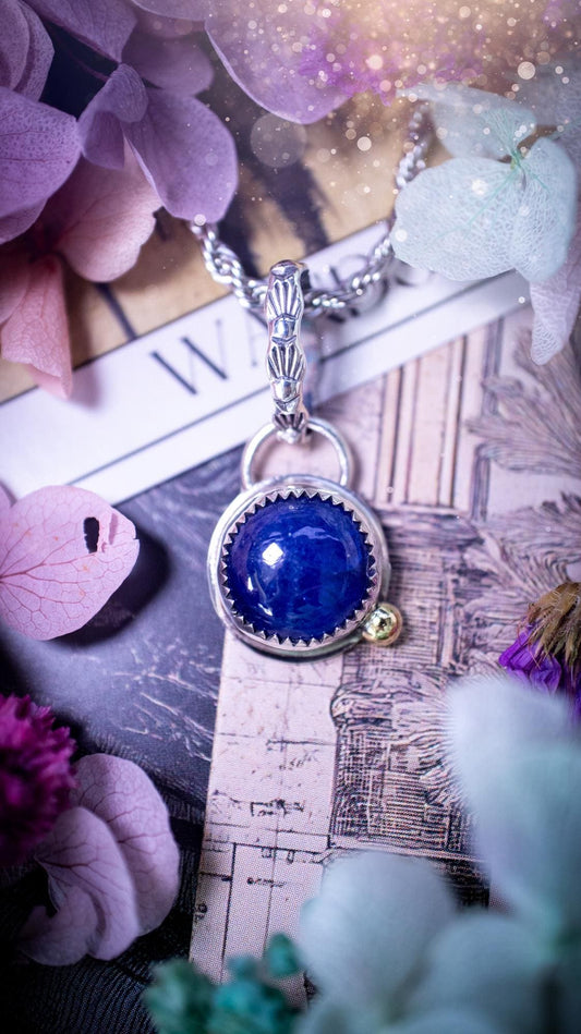 Handmade tanzanite pendant set in sterling silver with a high polished finish. The natural tanzanite gemstone displays rich blue violet tones with beautiful depth and shimmer in the light. Finished with a polished brass golden ball accent and a decorative patterned bail. Bohemian, gothic and witchy style crystal jewellery, perfect as a meaningful gift or elegant everyday statement piece. Tanzanite is the birthstone for December.