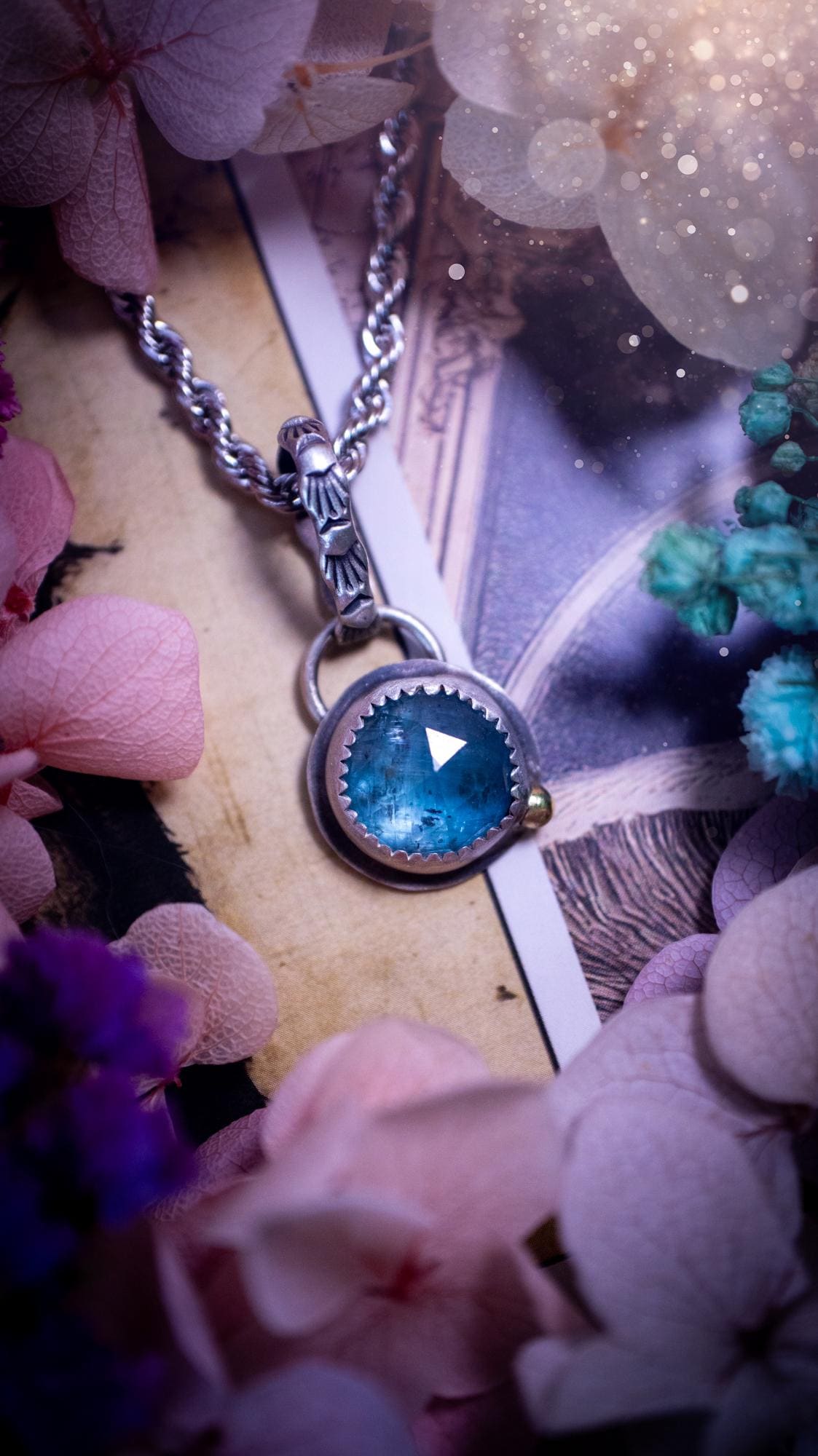 Handmade Paraiba kyanite pendant set in sterling silver with a satin brushed finish. The natural kyanite gemstone displays vibrant ocean-blue tones with a luminous glow. Finished with a polished brass golden ball accent and a decorative patterned bail. Bohemian, gothic and witchy style crystal jewellery, perfect as a unique gift or standout everyday piece