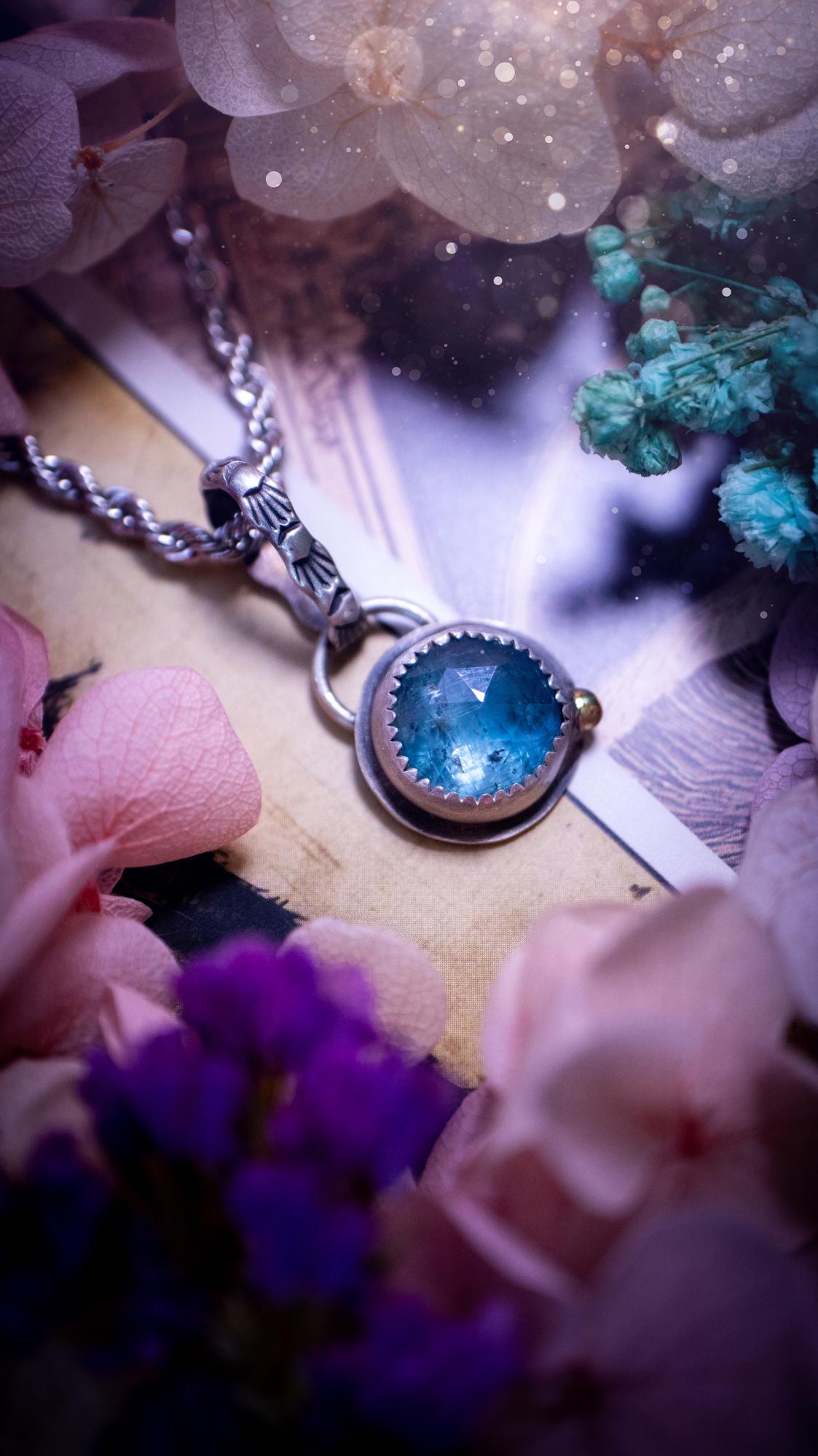 Handmade Paraiba kyanite pendant set in sterling silver with a satin brushed finish. The natural kyanite gemstone displays vibrant ocean-blue tones with a luminous glow. Finished with a polished brass golden ball accent and a decorative patterned bail. Bohemian, gothic and witchy style crystal jewellery, perfect as a unique gift or standout everyday piece
