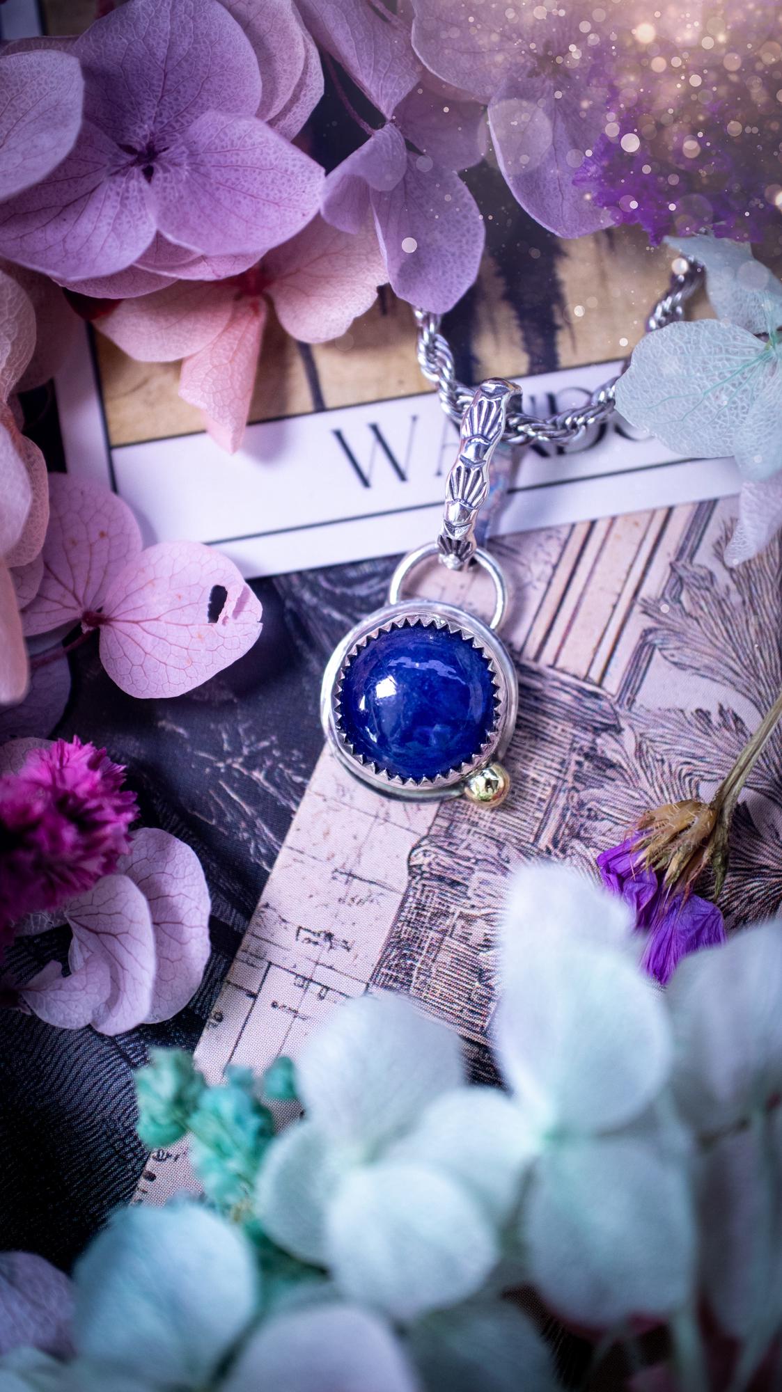 Handmade tanzanite pendant set in sterling silver with a high polished finish. The natural tanzanite gemstone displays rich blue violet tones with beautiful depth and shimmer in the light. Finished with a polished brass golden ball accent and a decorative patterned bail. Bohemian, gothic and witchy style crystal jewellery, perfect as a meaningful gift or elegant everyday statement piece. Tanzanite is the birthstone for December.