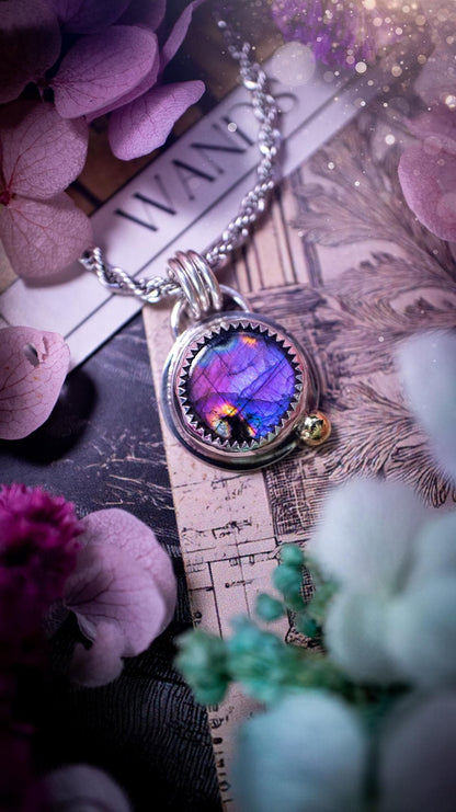 Handmade purple, rainbow labradorite pendant set in sterling silver with a high polished finish. The natural labradorite gemstone shows flashes of blue, gold and rainbow tones depending on the light. Features a polished brass golden ball accent and multi ring bail. Bohemian, gothic and witchy style crystal jewellery, perfect as a unique gift or everyday statement piece.