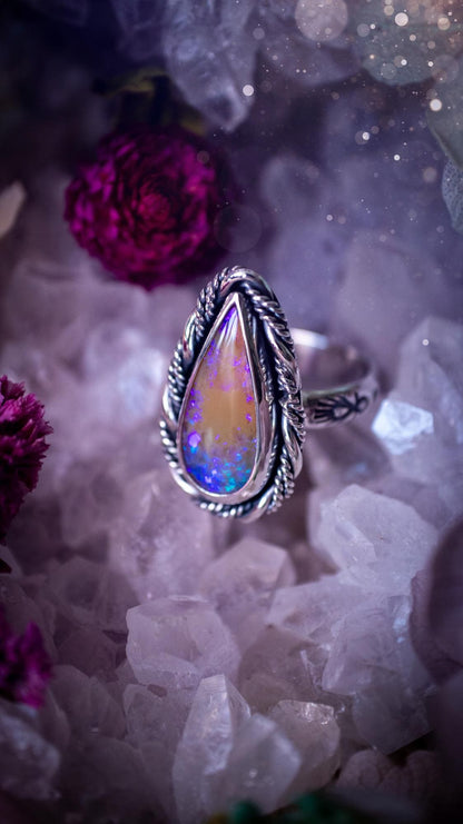 Handmade sterling silver and fine silver Australian opal ring displayed from an angled view. The natural opal shimmers with vivid pink, blue and purple colour play, surrounded by a smooth bezel setting. Decorative inner gallery wire and a hand-stamped patterned ring shank add artisan detail to this bold statement piece. UK size P, one-of-a-kind handmade jewellery.