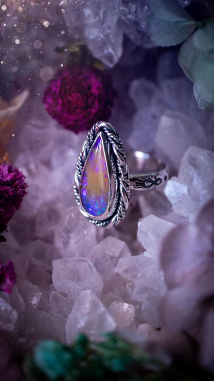 Close-up of a handmade Australian opal ring showing brilliant flashes of pink, blue and purple across the natural gemstone. The opal is securely set in a smooth fine silver bezel with intricate gallery wire detailing beneath. The sterling silver band features a decorative hand-stamped pattern, creating a bold and eye-catching statement ring perfect for opal lovers.