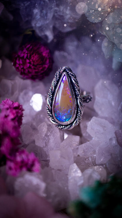 Handmade sterling silver and fine silver Australian opal ring displayed from an angled view. The natural opal shimmers with vivid pink, blue and purple colour play, surrounded by a smooth bezel setting. Decorative inner gallery wire and a hand-stamped patterned ring shank add artisan detail to this bold statement piece. UK size P, one-of-a-kind handmade jewellery.