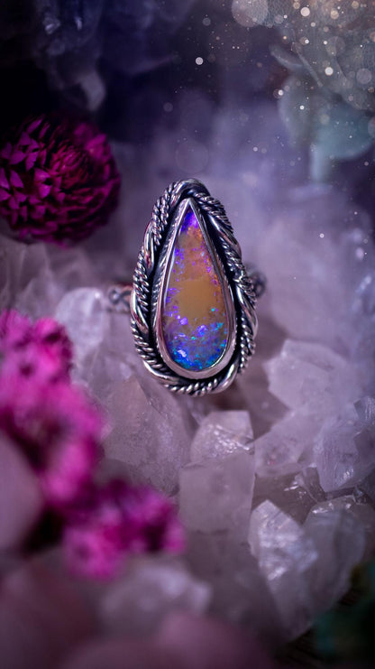 Close-up of a handmade Australian opal ring showing brilliant flashes of pink, blue and purple across the natural gemstone. The opal is securely set in a smooth fine silver bezel with intricate gallery wire detailing beneath. The sterling silver band features a decorative hand-stamped pattern, creating a bold and eye-catching statement ring perfect for opal lovers.