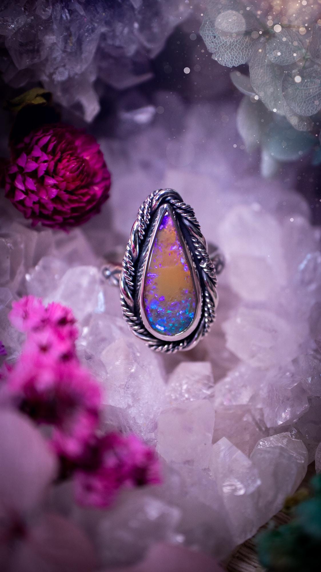 Close-up of a handmade Australian opal ring showing brilliant flashes of pink, blue and purple across the natural gemstone. The opal is securely set in a smooth fine silver bezel with intricate gallery wire detailing beneath. The sterling silver band features a decorative hand-stamped pattern, creating a bold and eye-catching statement ring perfect for opal lovers.
