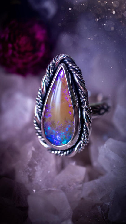 Handmade sterling silver and fine silver Australian opal ring displayed from an angled view. The natural opal shimmers with vivid pink, blue and purple colour play, surrounded by a smooth bezel setting. Decorative inner gallery wire and a hand-stamped patterned ring shank add artisan detail to this bold statement piece. UK size P, one-of-a-kind handmade jewellery.