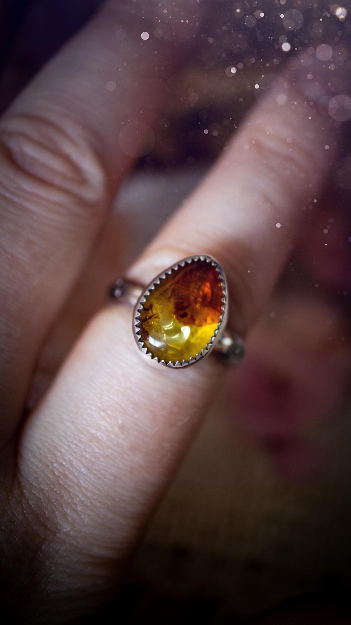 Handmade amber ring crafted from fine silver and sterling silver featuring a warm golden amber gemstone set in a decorative serrated bezel. The artisan ring showcases a signature patterned silver band with intricate detailing. Size UK O 1/2. A unique bohemian statement ring inspired by nature, displaying the rich honey tones and natural glow of genuine fossilised amber. Perfect handmade gemstone jewellery gift for crystal and silver jewellery lovers.