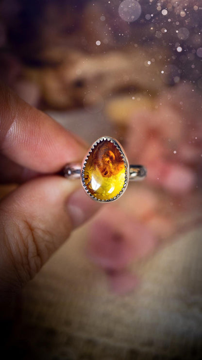 Handmade amber ring crafted from fine silver and sterling silver featuring a warm golden amber gemstone set in a decorative serrated bezel. The artisan ring showcases a signature patterned silver band with intricate detailing. Size UK O 1/2. A unique bohemian statement ring inspired by nature, displaying the rich honey tones and natural glow of genuine fossilised amber. Perfect handmade gemstone jewellery gift for crystal and silver jewellery lovers.