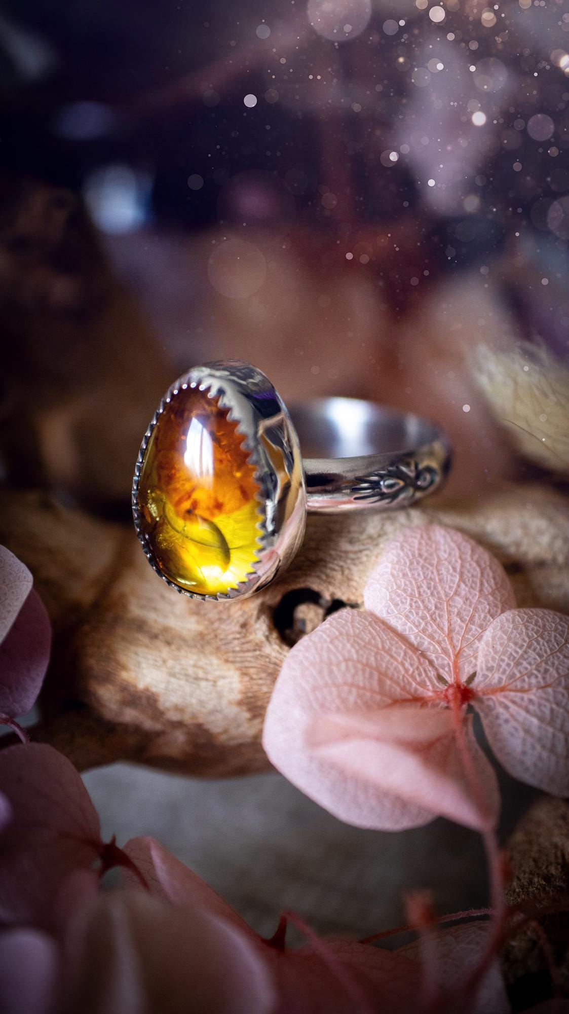 Handmade amber ring crafted from fine silver and sterling silver featuring a warm golden amber gemstone set in a decorative serrated bezel. The artisan ring showcases a signature patterned silver band with intricate detailing. Size UK O 1/2. A unique bohemian statement ring inspired by nature, displaying the rich honey tones and natural glow of genuine fossilised amber. Perfect handmade gemstone jewellery gift for crystal and silver jewellery lovers.