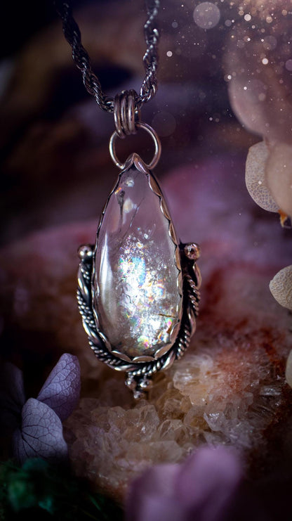 Handmade white topaz pendant necklace crafted from fine silver and sterling silver. The teardrop white topaz gemstone displays stunning natural cluster rainbows and subtle sparkle within the stone. The elegant silver setting highlights the crystal's unique inclusions and clarity. Photographed against a neutral background, this artisan gemstone necklace makes a thoughtful November birthstone gift. A necklace that is the definition of celestial and fairycore!