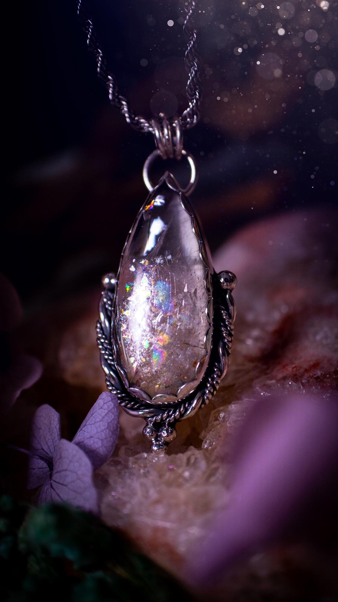Handmade white topaz pendant necklace crafted from fine silver and sterling silver. The teardrop white topaz gemstone displays stunning natural cluster rainbows and subtle sparkle within the stone. The elegant silver setting highlights the crystal's unique inclusions and clarity. Photographed against a neutral background, this artisan gemstone necklace makes a thoughtful November birthstone gift. A necklace that is the definition of celestial and fairycore!