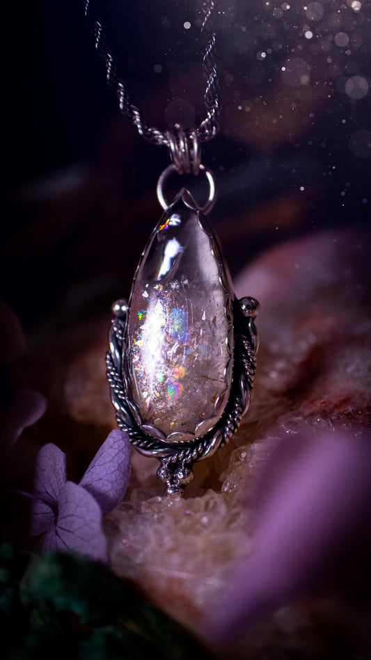 Handmade white topaz pendant necklace crafted from fine silver and sterling silver. The teardrop white topaz gemstone displays stunning natural cluster rainbows and subtle sparkle within the stone. The elegant silver setting highlights the crystal's unique inclusions and clarity. Photographed against a neutral background, this artisan gemstone necklace makes a thoughtful November birthstone gift. A necklace that is the definition of celestial and fairycore!