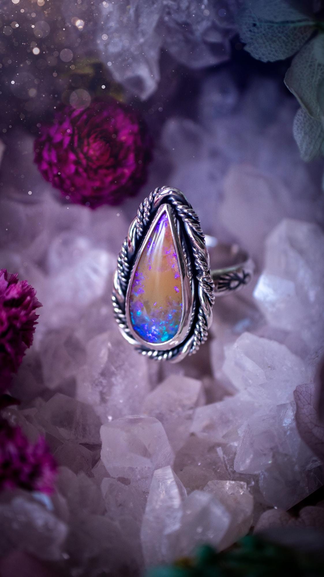 Close-up of a handmade Australian opal ring showing brilliant flashes of pink, blue and purple across the natural gemstone. The opal is securely set in a smooth fine silver bezel with intricate gallery wire detailing beneath. The sterling silver band features a decorative hand-stamped pattern, creating a bold and eye-catching statement ring perfect for opal lovers.