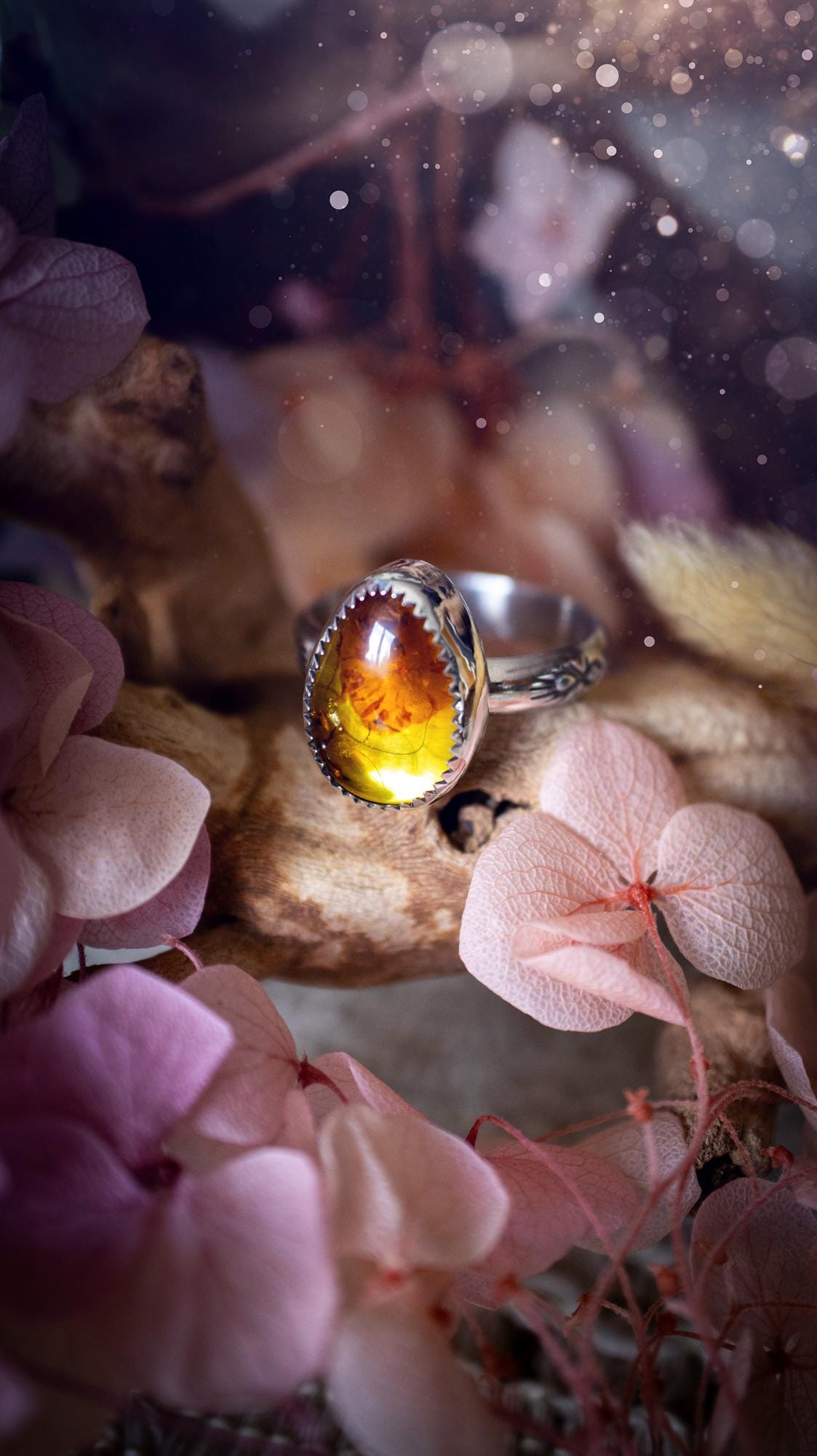 Handmade amber ring crafted from fine silver and sterling silver featuring a warm golden amber gemstone set in a decorative serrated bezel. The artisan ring showcases a signature patterned silver band with intricate detailing. Size UK O 1/2. A unique bohemian statement ring inspired by nature, displaying the rich honey tones and natural glow of genuine fossilised amber. Perfect handmade gemstone jewellery gift for crystal and silver jewellery lovers.