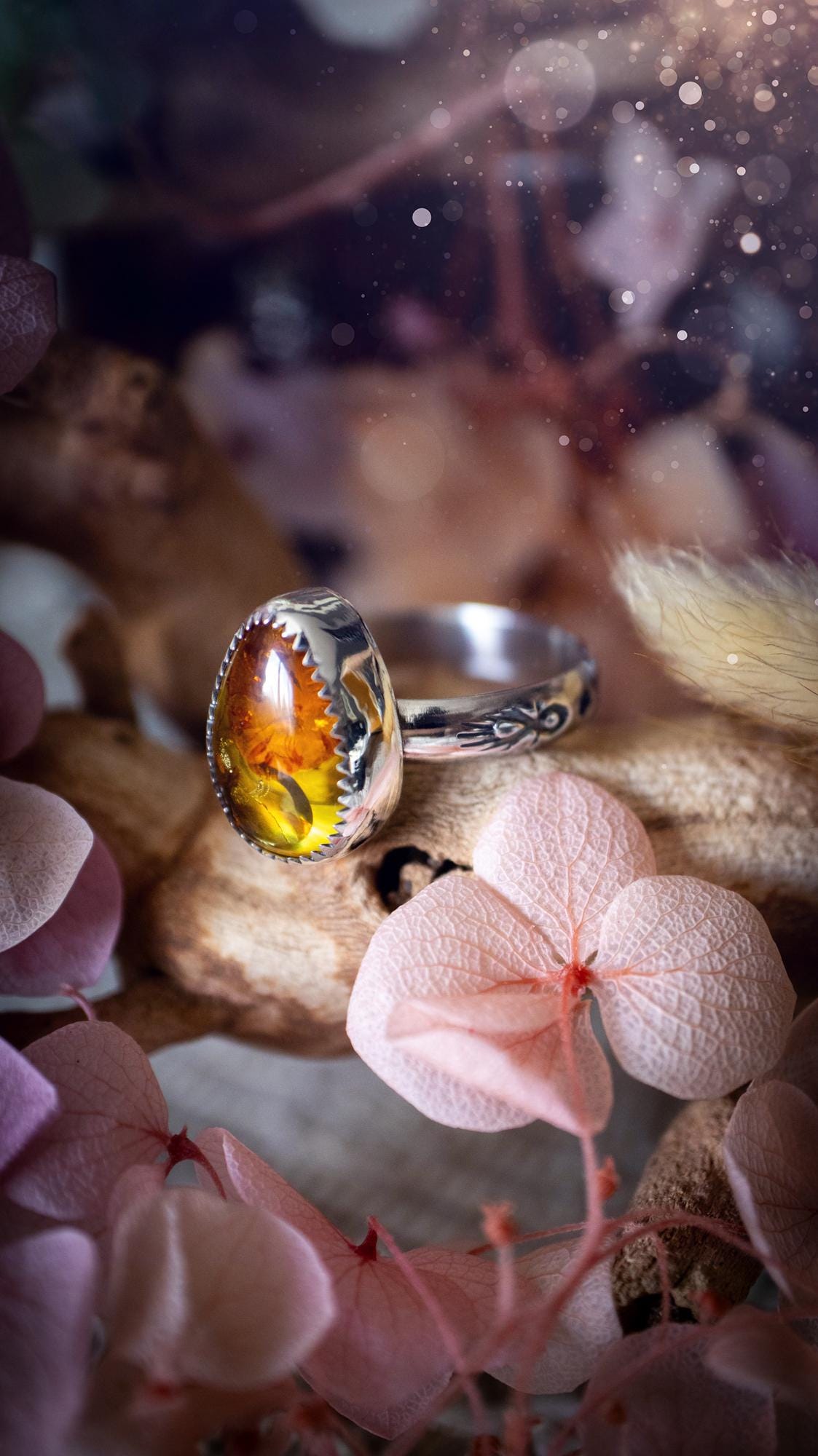 Handmade amber ring crafted from fine silver and sterling silver featuring a warm golden amber gemstone set in a decorative serrated bezel. The artisan ring showcases a signature patterned silver band with intricate detailing. Size UK O 1/2. A unique bohemian statement ring inspired by nature, displaying the rich honey tones and natural glow of genuine fossilised amber. Perfect handmade gemstone jewellery gift for crystal and silver jewellery lovers.